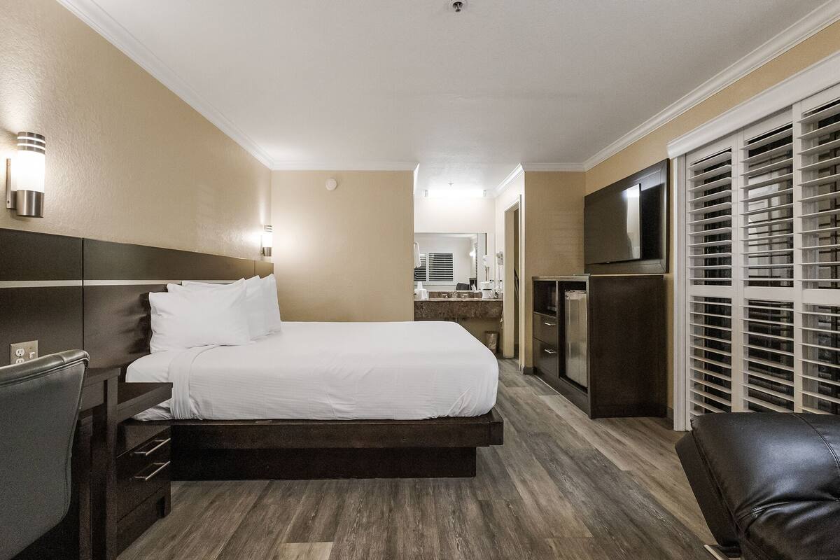 A hotel room with a bed, a desk, a mirror, a TV, and a closet with sliding doors.