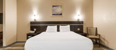 A hotel room with a large bed, two bedside lamps, a chair, and a painting on the wall.