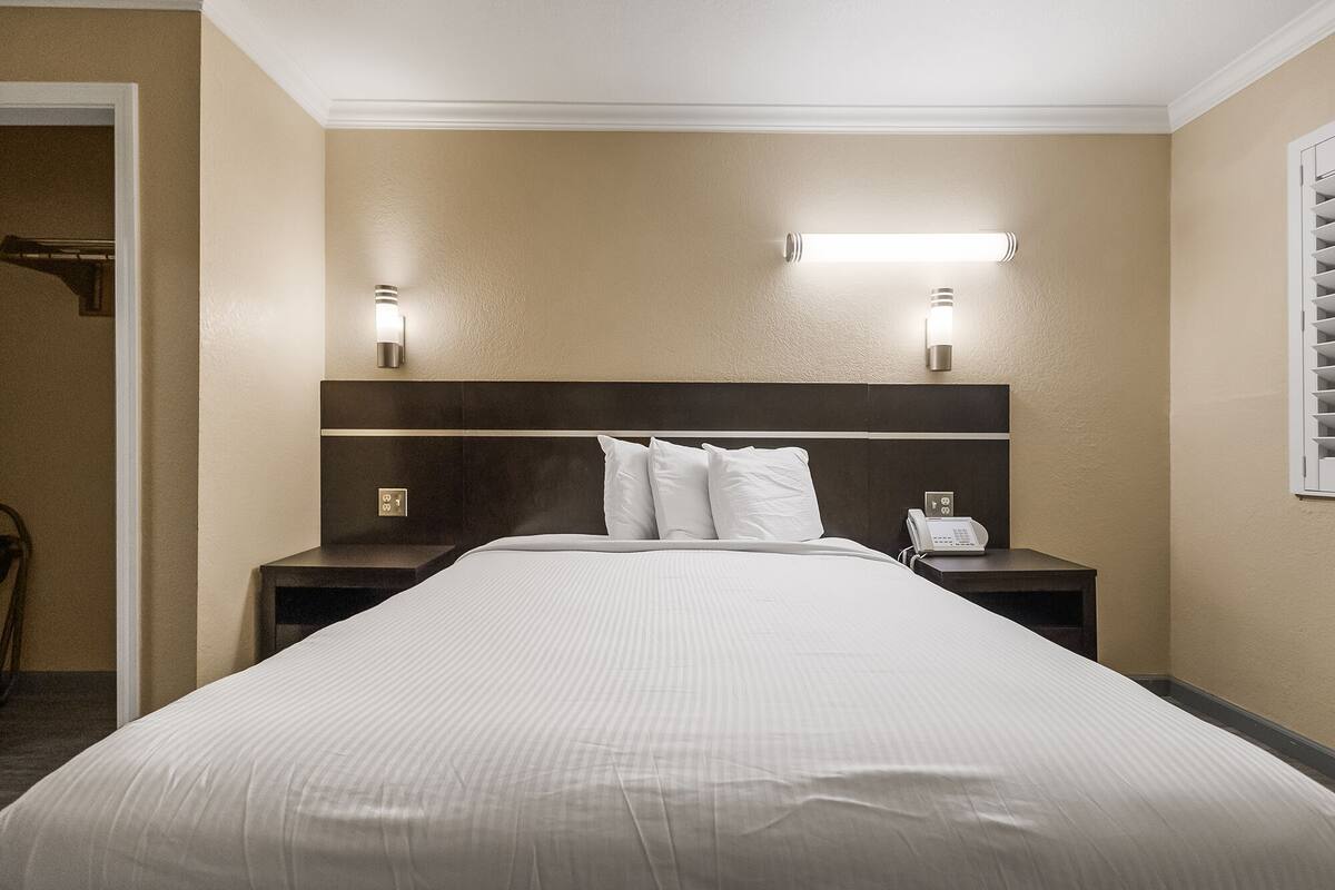 A hotel room with a large bed, two bedside tables, a phone, and wall-mounted lights.