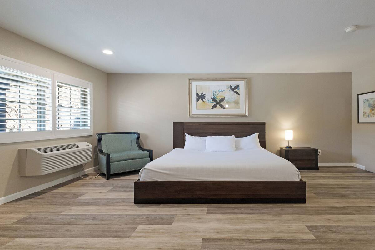 A bedroom with a large bed, a chair, a nightstand, and artwork on the walls.