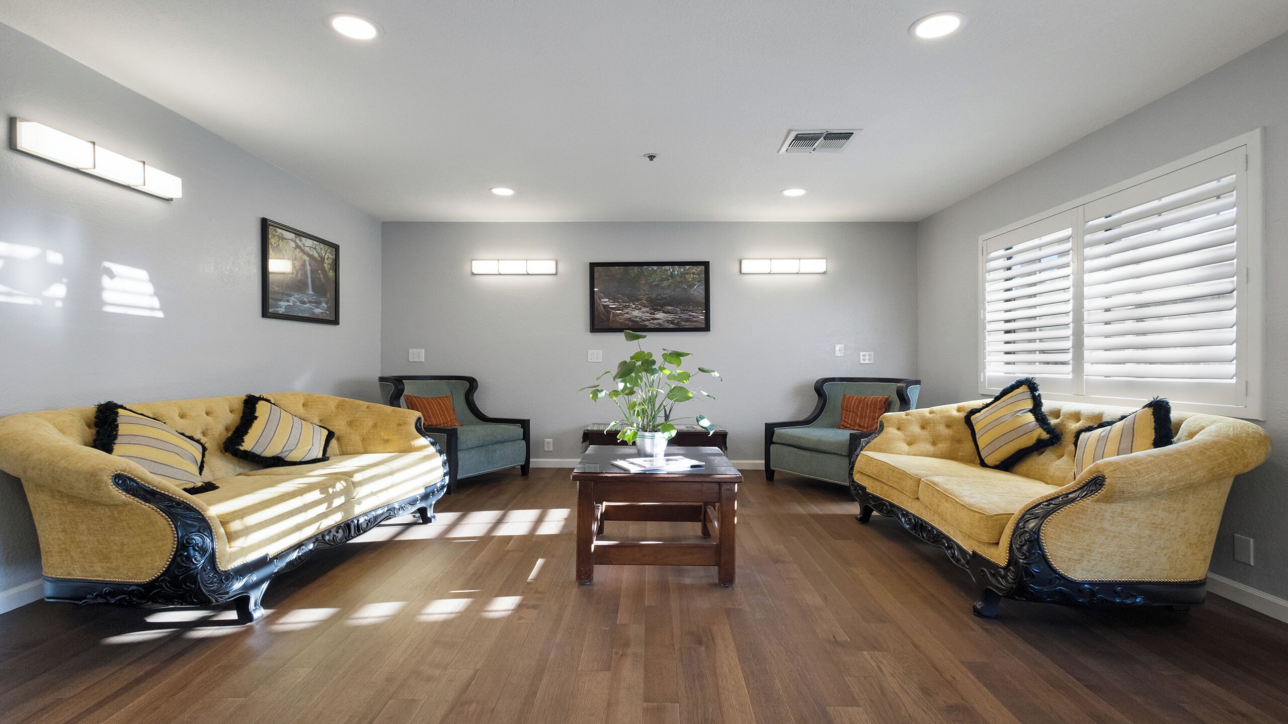 Un salón amplio con dos sofás amarillos, una mesa de centro de madera y un ventanal con persianas.