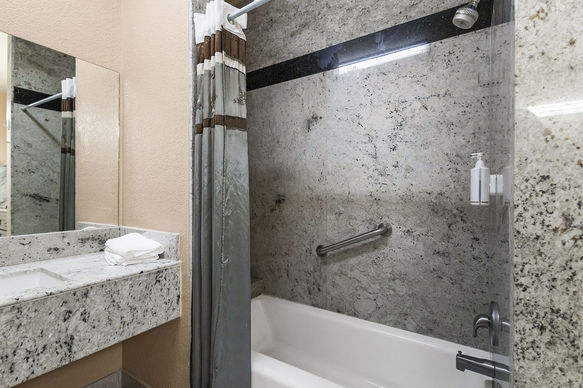 A bathroom with a granite countertop, a white bathtub, a shower with a handheld showerhead, and a towel rack.