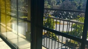 A balcony with a metal railing, a view of a parking area, and a forested hill in the background. - Country Inn Sonora (Jamestown)