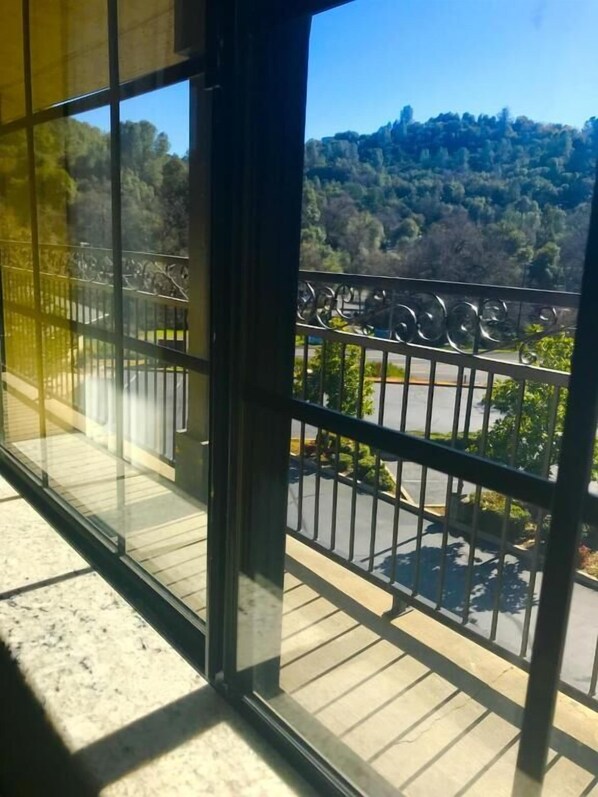 Un balcone con ringhiera metallica, vista su un'area di parcheggio e una collina boscosa sullo sfondo.