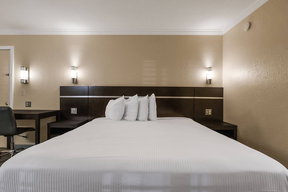 A hotel room with a large bed, two bedside tables, a chair, and wall-mounted lighting.