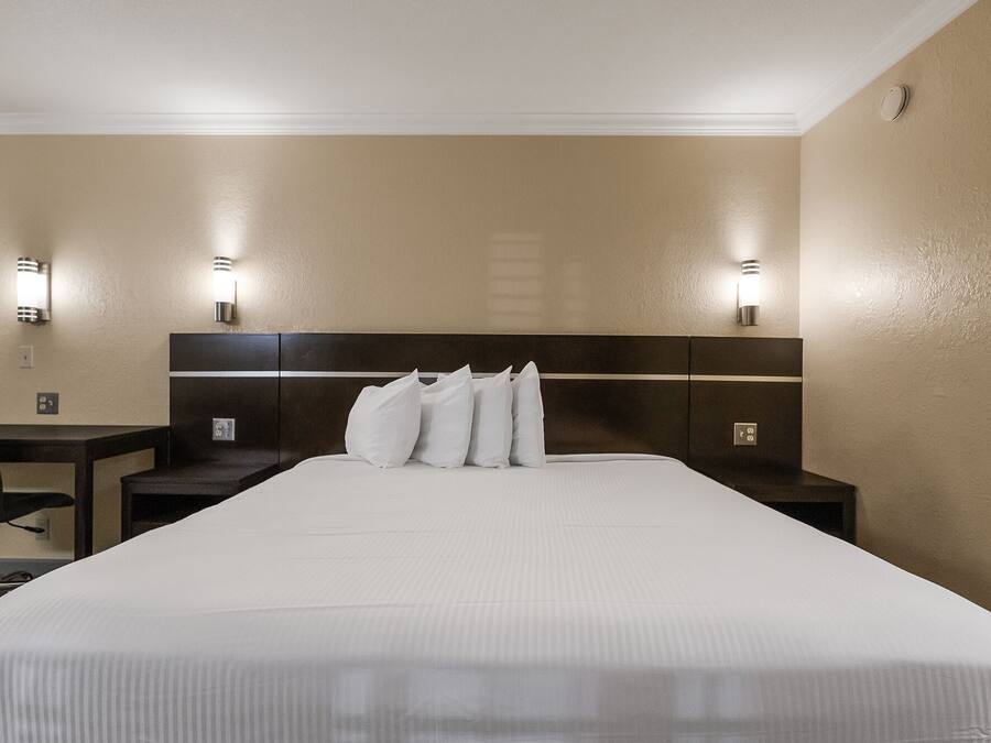A hotel room with a large bed, two bedside tables, a chair, and wall-mounted lighting.