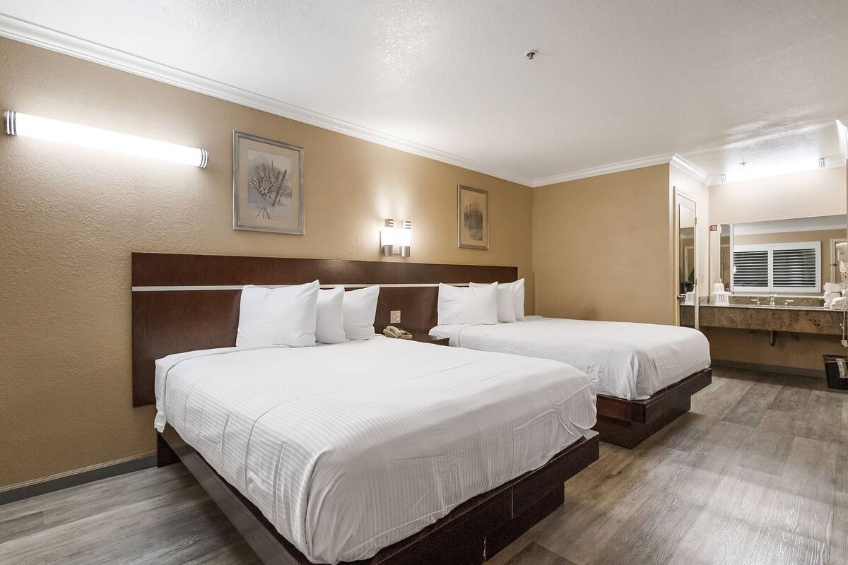 A hotel room with two beds, a large mirror, and a bathroom with a sink and toilet.