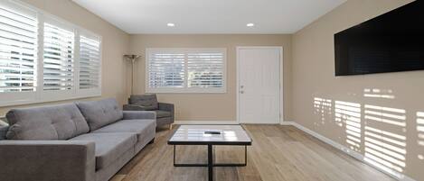 A modern living room with a grey sofa, a coffee table, and a TV mounted on the wall.