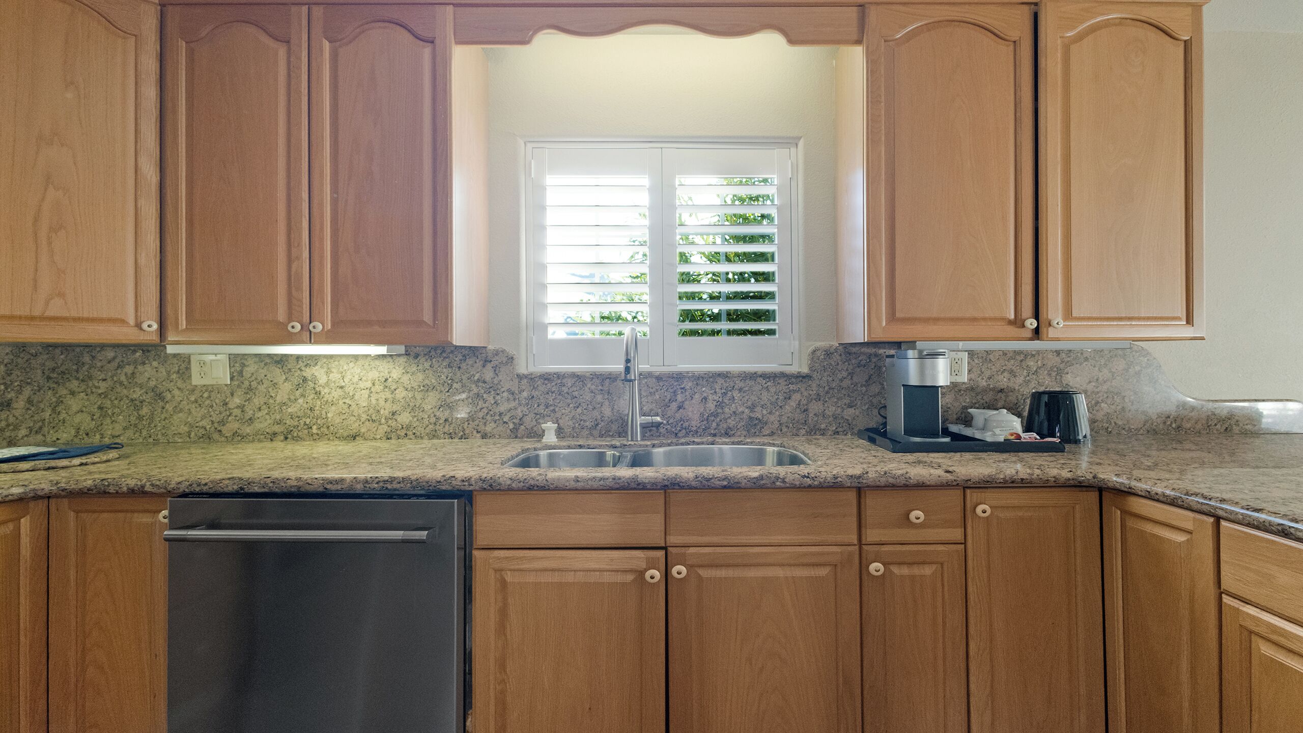 A kitchen with wooden cabinets, a stainless steel sink, and a coffee maker.