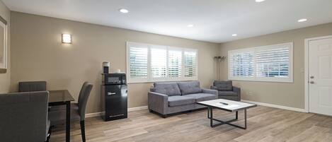 A modern living room with a grey sofa, a coffee machine, and a dining area with a table and chairs.