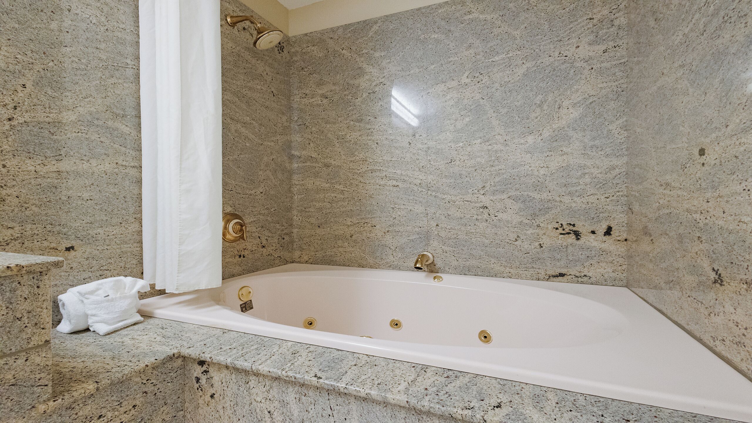 A bathroom with a freestanding bathtub, marble walls, and a towel on the floor.