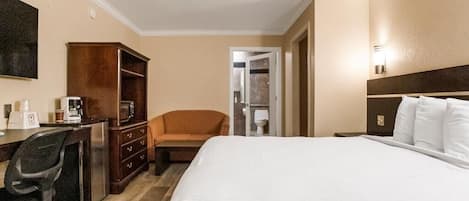 A hotel room with a bed, a desk with a chair, a wardrobe, and a television on the wall.