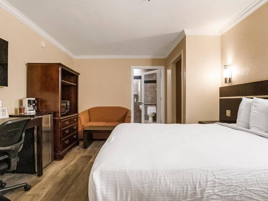 A hotel room with a bed, a desk with a chair, a wardrobe, and a television on the wall.