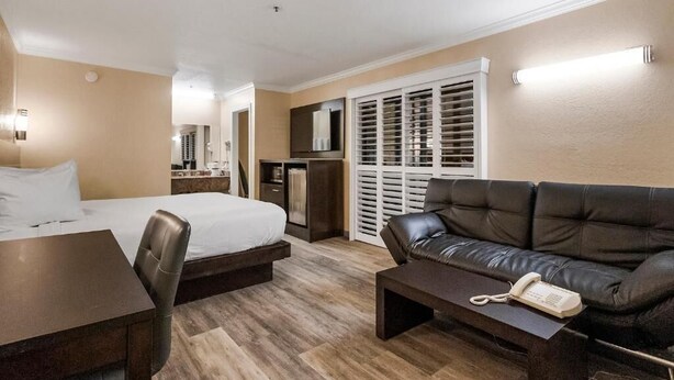A hotel room with a bed, a desk, a leather sofa, a telephone, and a wardrobe with sliding doors. - Country Inn Sonora (Jamestown)