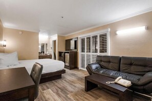A hotel room with a bed, a desk, a leather sofa, a telephone, and a wardrobe with sliding doors. - Country Inn Sonora (Jamestown)