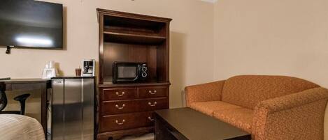 Quarto de hotel compacto com cozinha compacta, televisão de tela plana, sofá e uma mesa pequena.