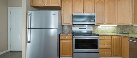A kitchen with wooden cabinets, a stainless steel refrigerator, a microwave, and an oven.
