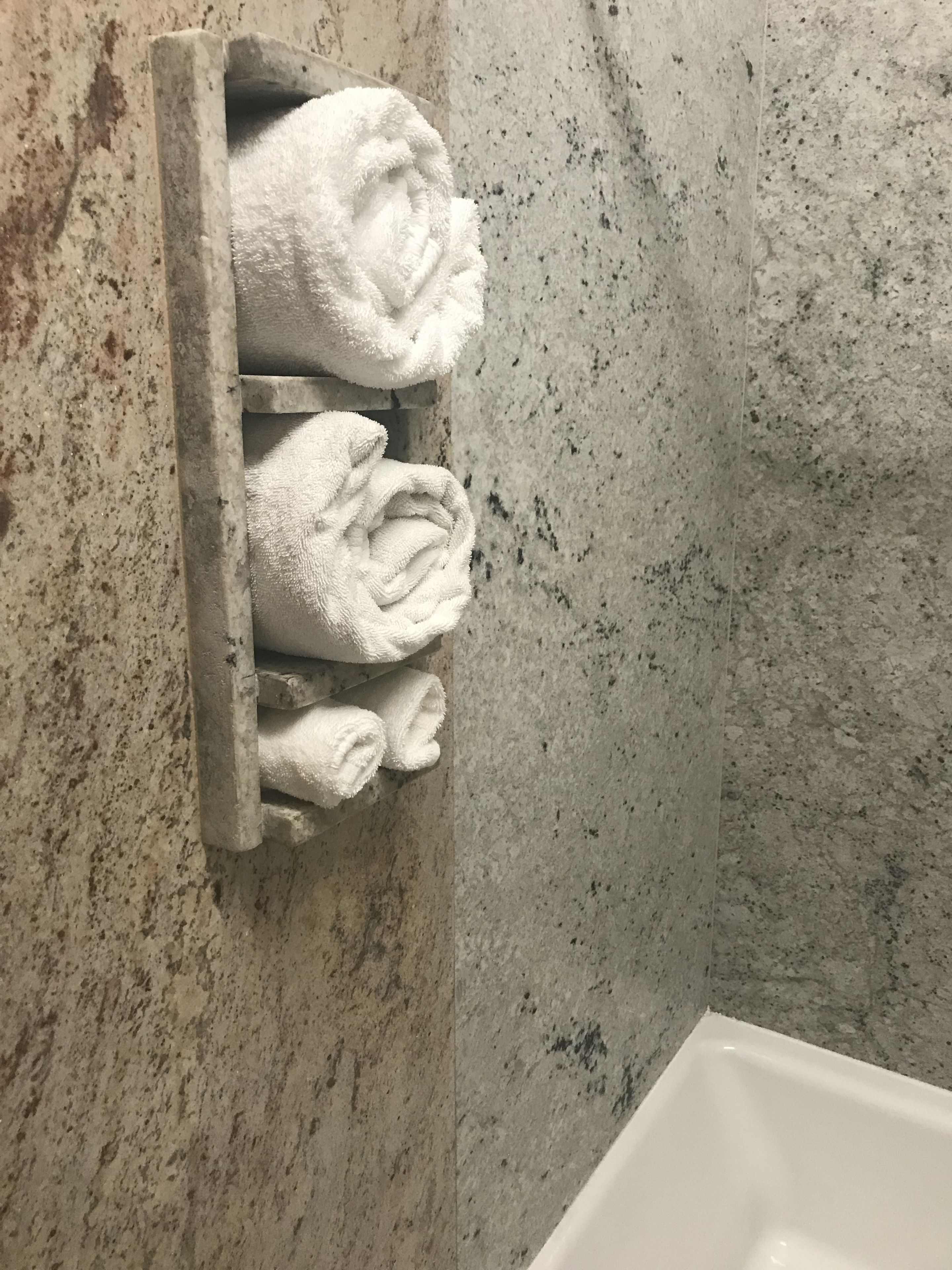A bathroom with a marble wall and a built-in towel rack holding several folded towels.