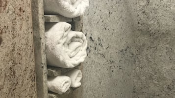 A bathroom with a marble wall and a built-in towel rack holding several folded towels.