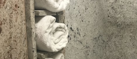 A bathroom with a marble wall and a built-in towel rack holding several folded towels.