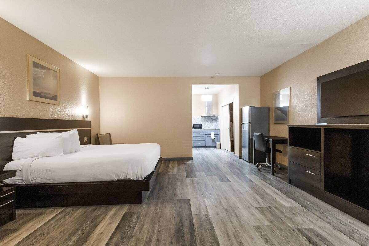 A hotel room with a bed, a desk, a television, and a kitchenette.