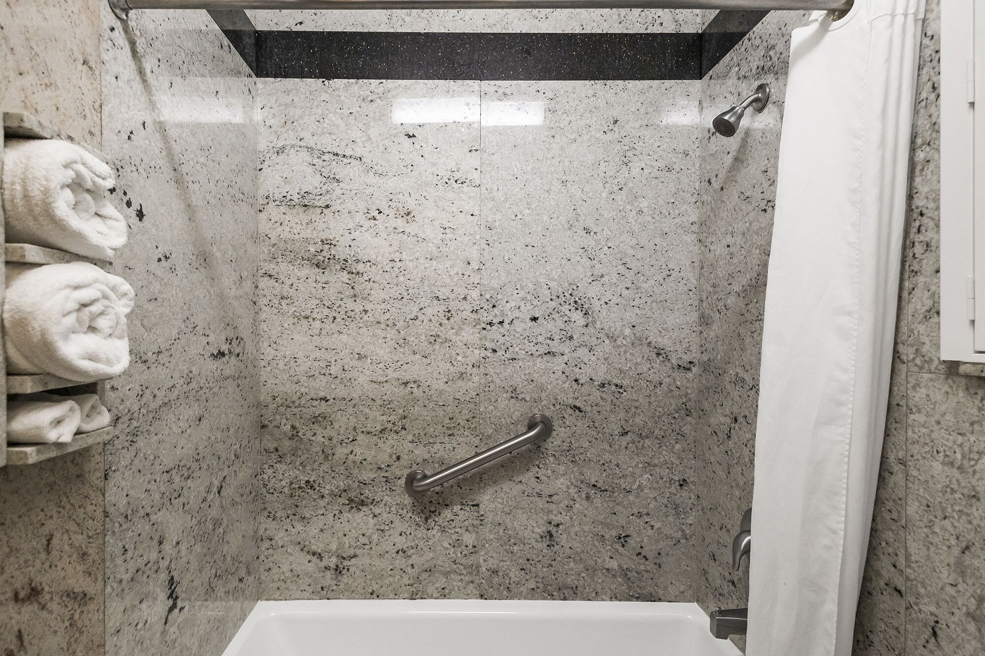 Une douche avec un pommeau de douche amovible, un porte-serviettes avec des serviettes pliées et un rideau de douche.