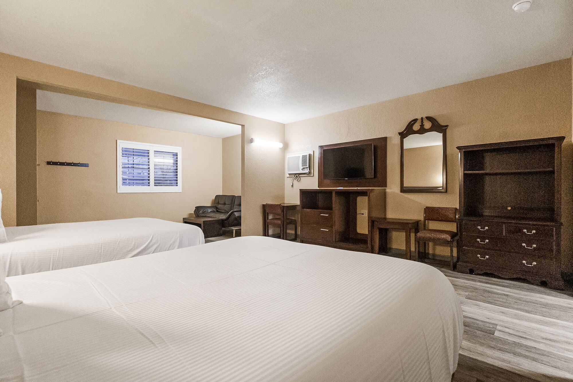 A hotel room with two beds, a desk, a chair, a TV, and a dresser.