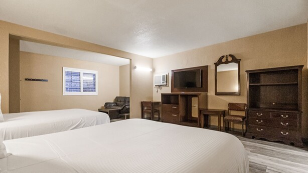 A hotel room with two beds, a desk, a chair, a TV, and a dresser.
