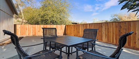 Un patio al aire libre con una mesa y cuatro sillas, rodeado por una valla de madera y un árbol.