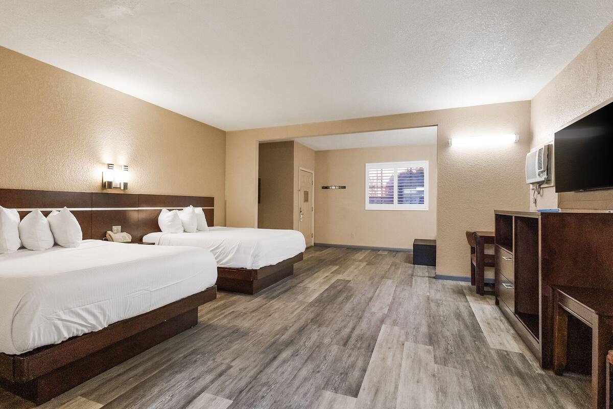 A hotel room with two beds, a television, and a desk.