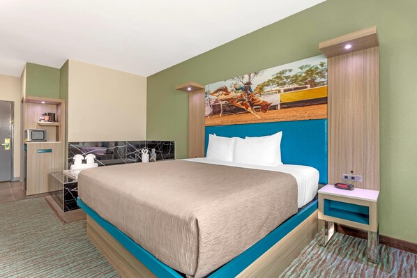 A hotel room with a large bed, a small desk, a mirror, and a painting on the wall.