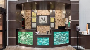 A reception area with a 'Quality by Choice Hotels' sign, a reception desk, and a wall with framed awards.