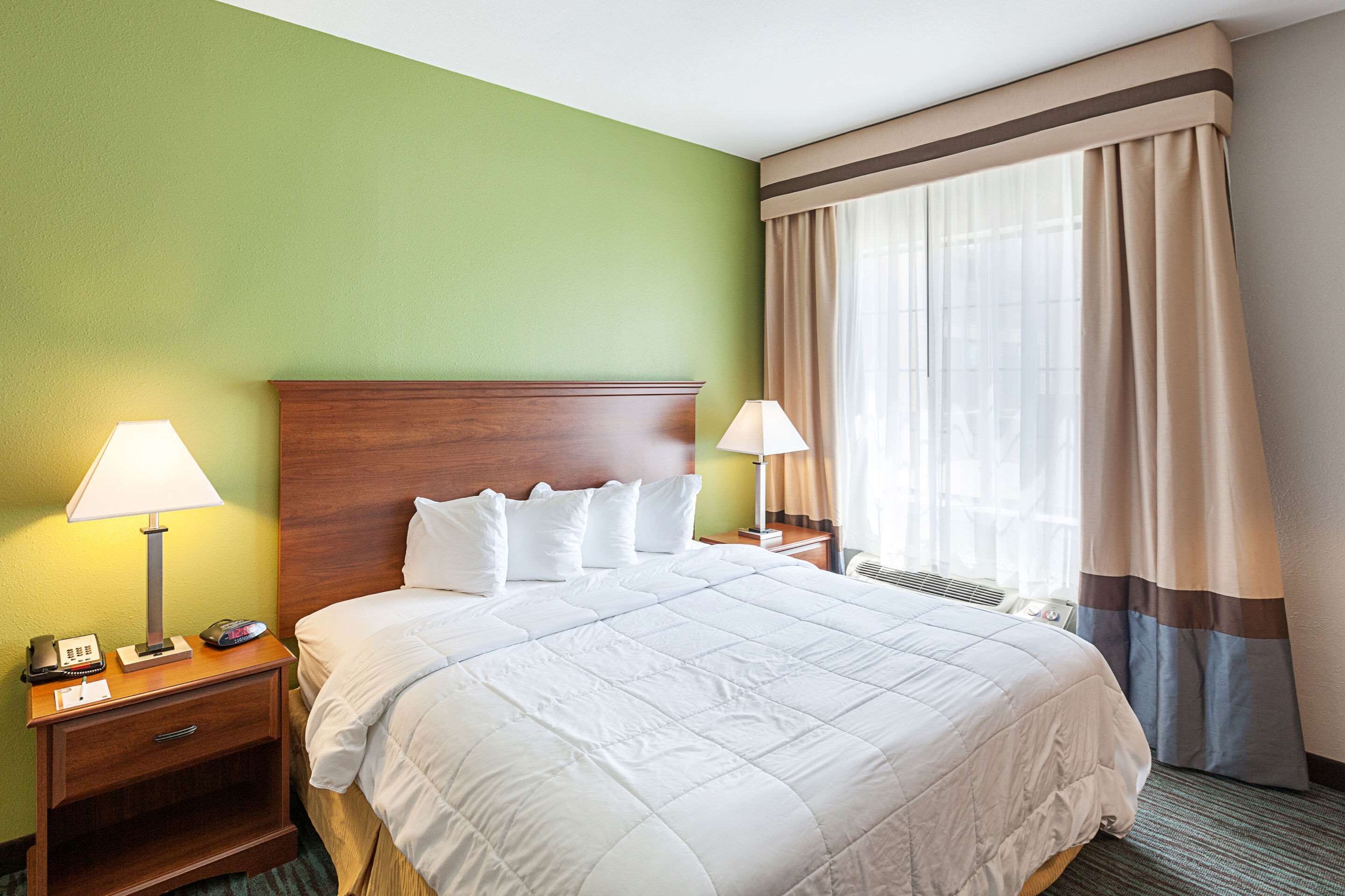 Une chambre d’hôtel avec un grand lit, deux tables de chevet avec des lampes, un téléphone et une fenêtre avec des rideaux.