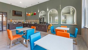 A modern kitchen with a microwave, sink, and counter space. There are orange and blue chairs around tables.
