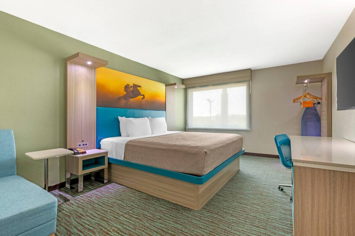 Ein Hotelzimmer mit Bett, Schreibtisch, Stuhl, einem kleinen Tisch und einem Bild an der Wand.