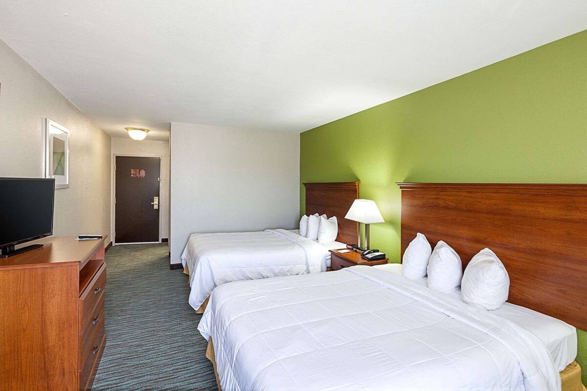 Ein Hotelzimmer mit zwei Betten, einem Fernseher, einem Schreibtisch und einer Lampe.