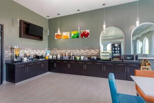 Una cocina moderna con armarios oscuros, una encimera con varios electrodomésticos y una zona de comedor con sillas azules.