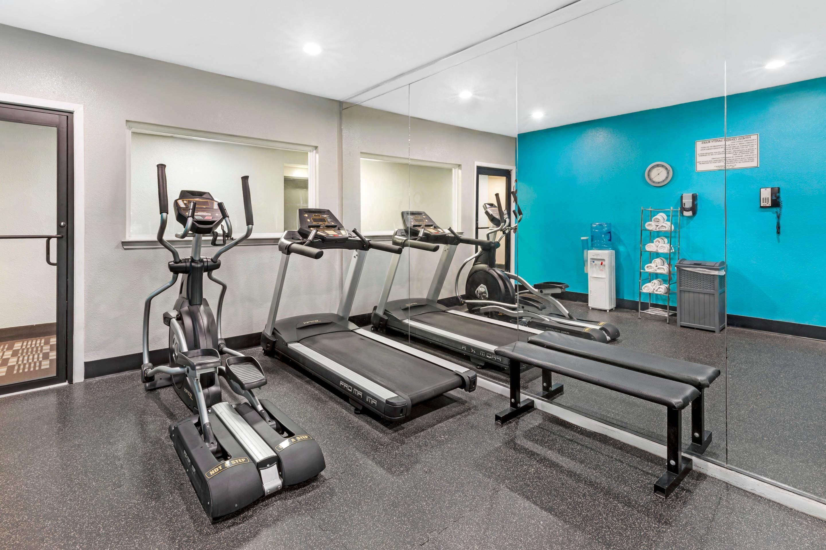 Ein Fitnessraum mit Laufbändern, Crosstrainern und einer Bank.