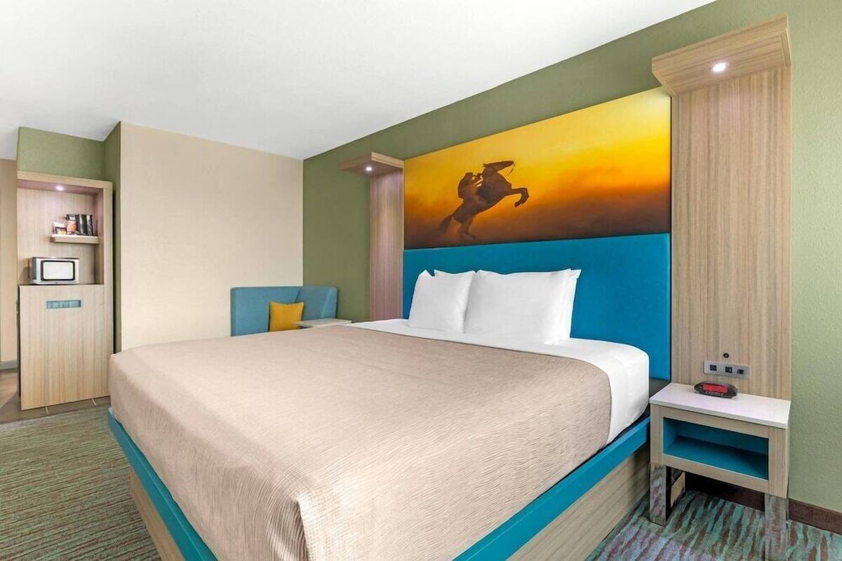 Ein Hotelzimmer mit Bett, Nachttisch, Fernseher und einem Bild an der Wand.