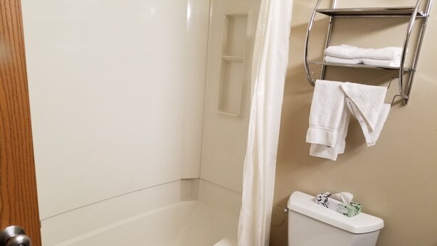 A bathroom with a bathtub, toilet, and a towel rack with towels. - Prairie Inn (Vermillion)
