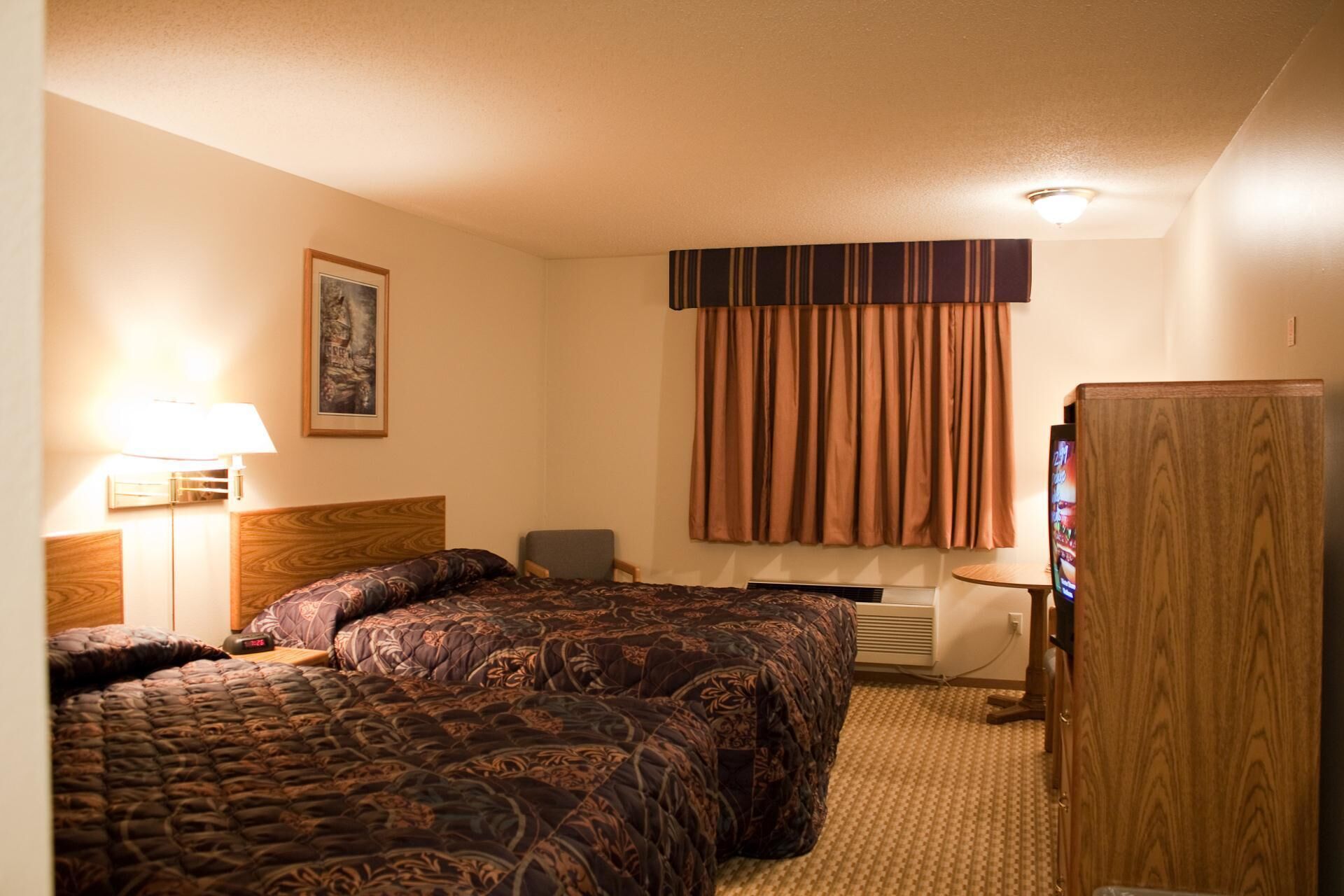 A hotel room with two beds, a desk, a chair, a television, and a wardrobe.