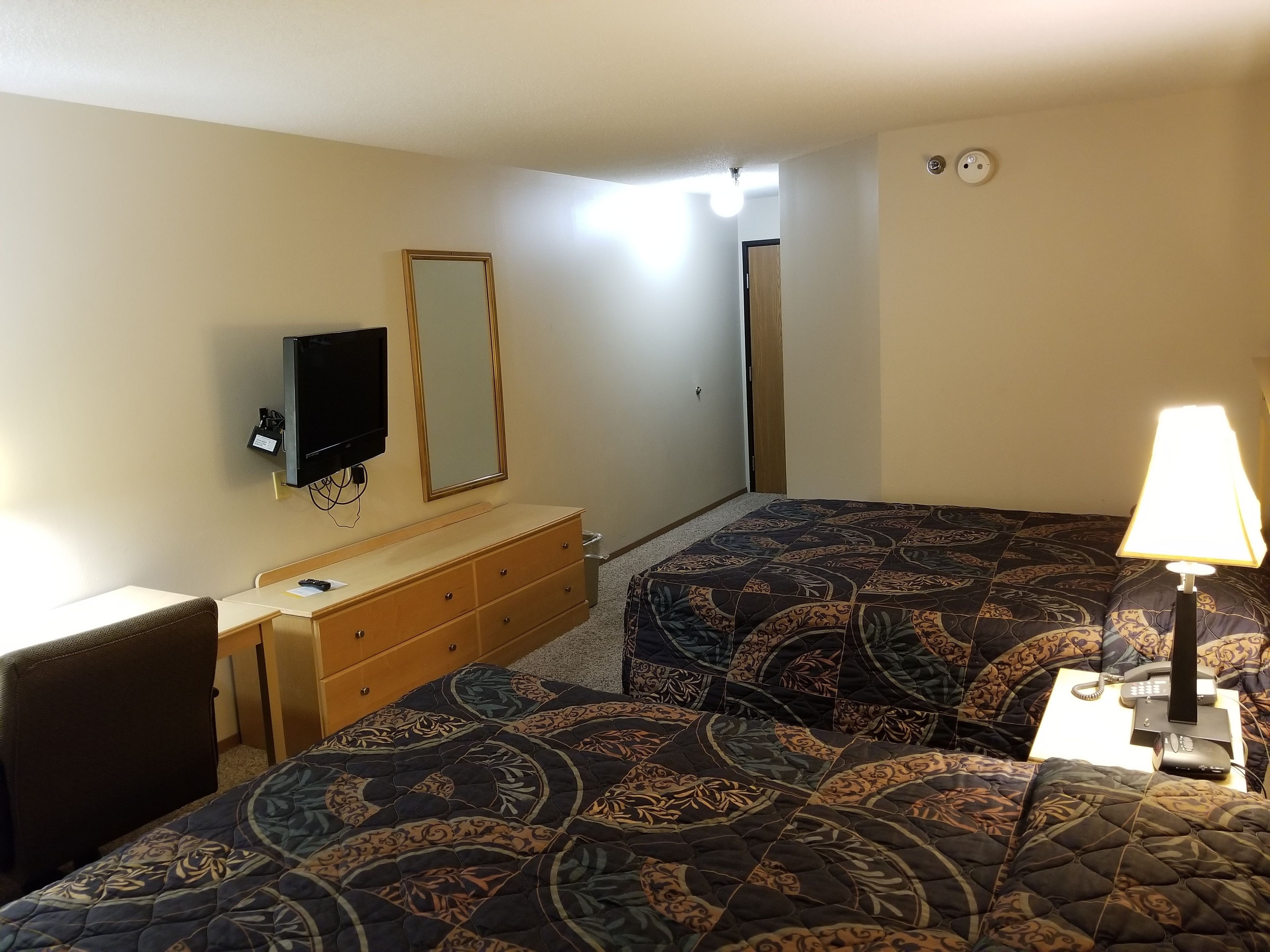 Una habitación de hotel con dos camas, un aparador, un televisor y una lámpara.