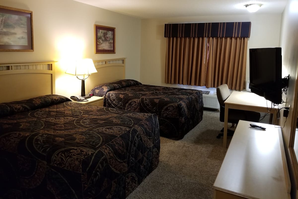 Een hotelkamer met twee bedden, een bureau, een televisie en een lamp.