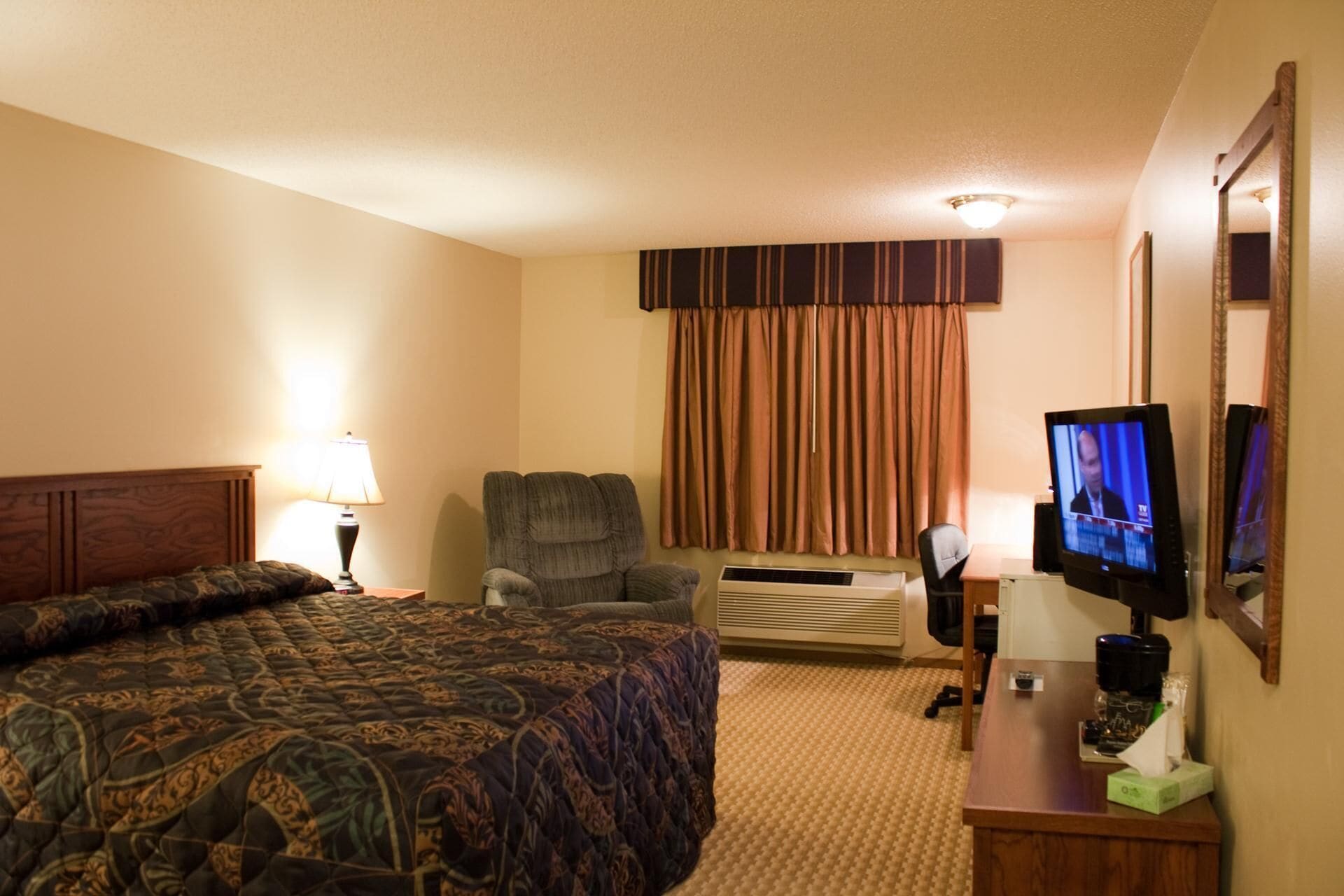 Habitación de hotel con una cama grande, una silla, un escritorio con computadora y televisión.