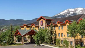 A hotel with a stone facade, red accents, and a mountain backdrop. - Comfort Suites Summit County (Dillon)