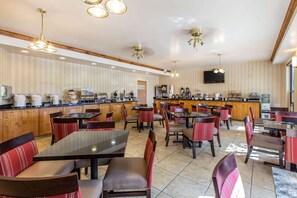 A spacious restaurant with multiple tables and booths, a counter with a variety of food and drink options, and a television mounted on the wall.