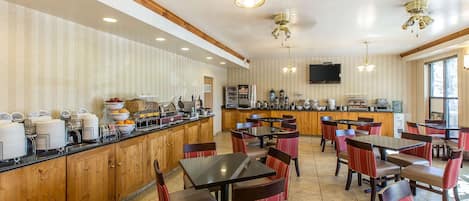 A spacious dining area with multiple tables and chairs, a kitchen area with various appliances, and a large window providing natural light.
