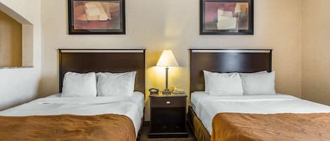 A hotel room with two beds, a nightstand with a lamp, and abstract art on the walls.