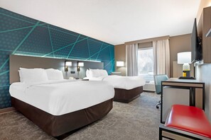 A hotel room with two beds, a desk, a chair, a TV, and a window with curtains.