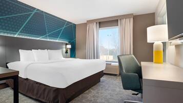 A hotel room with a large bed, a desk, a chair, a window with curtains, and a wall with a geometric pattern.